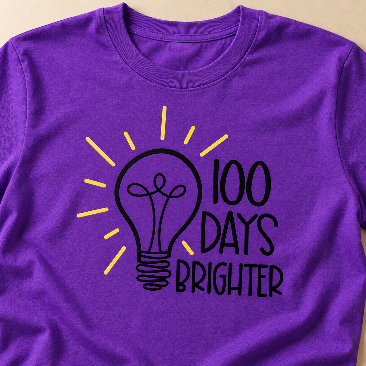 Close-up of the 100 Days Brighter lightbulb design printed on a purple tee